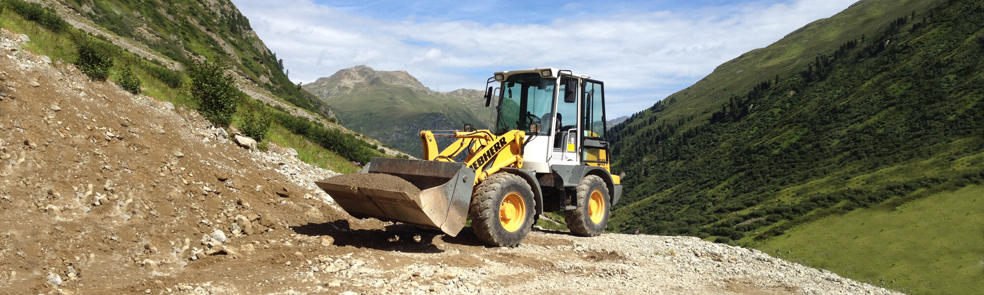 Gelber Liebherr-Radlader auf steiniger Baustelle in bergiger Umgebung.